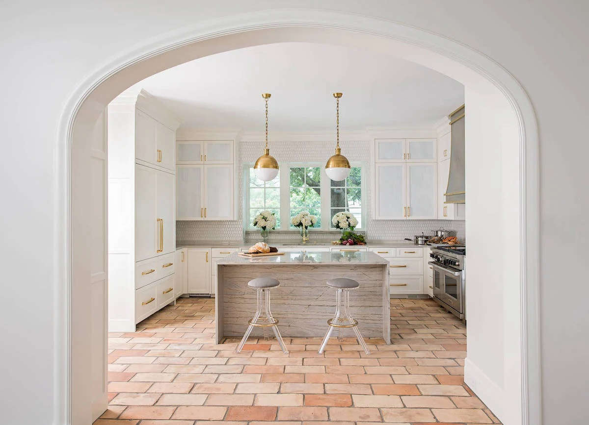 cucina classica bianca con isola centrale in legno e top in vetro maniglie giallo oro e pavimento in cotto